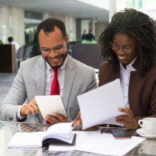 Cheerful business colleagues checking documents during coffee break. Business man and woman sitting in cafe, reading documents and using tablet. Paperwork concept